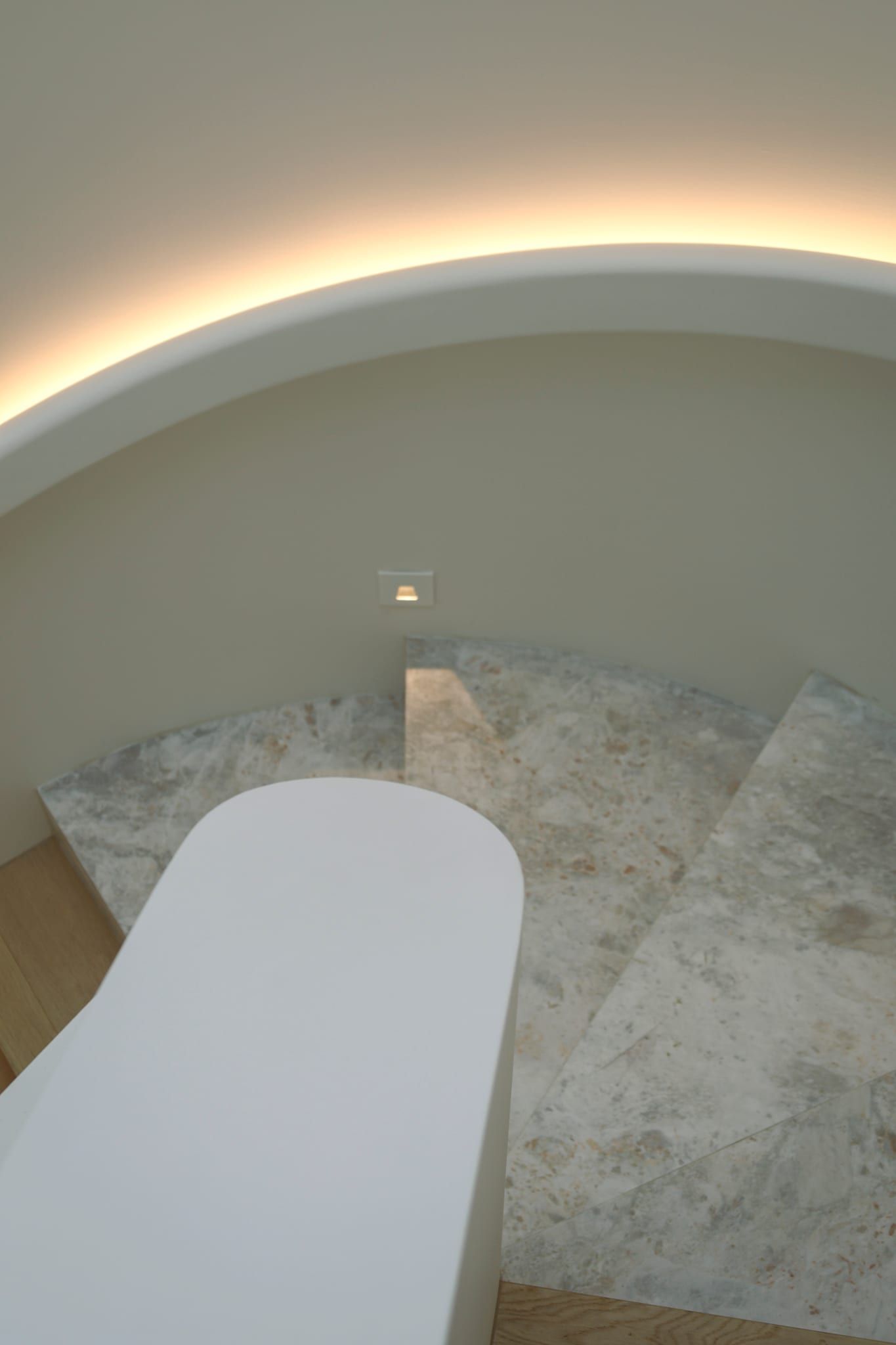 Looking down the curved stair, stone treads beneath a cove-lit ceiling