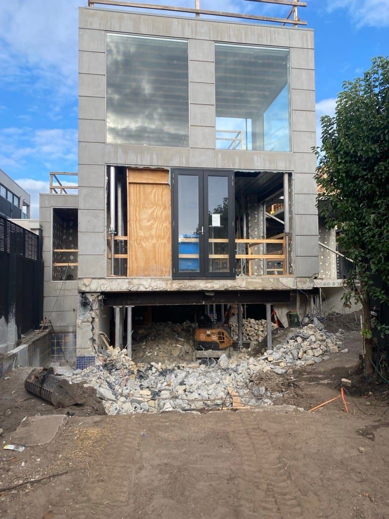 The propped structure front on, three storeys held above the cleared ground