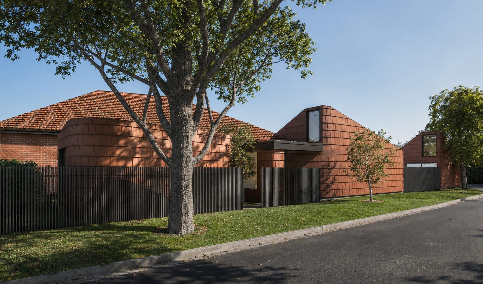 The new shingle-clad forms stepping along the street behind the original terracotta roof